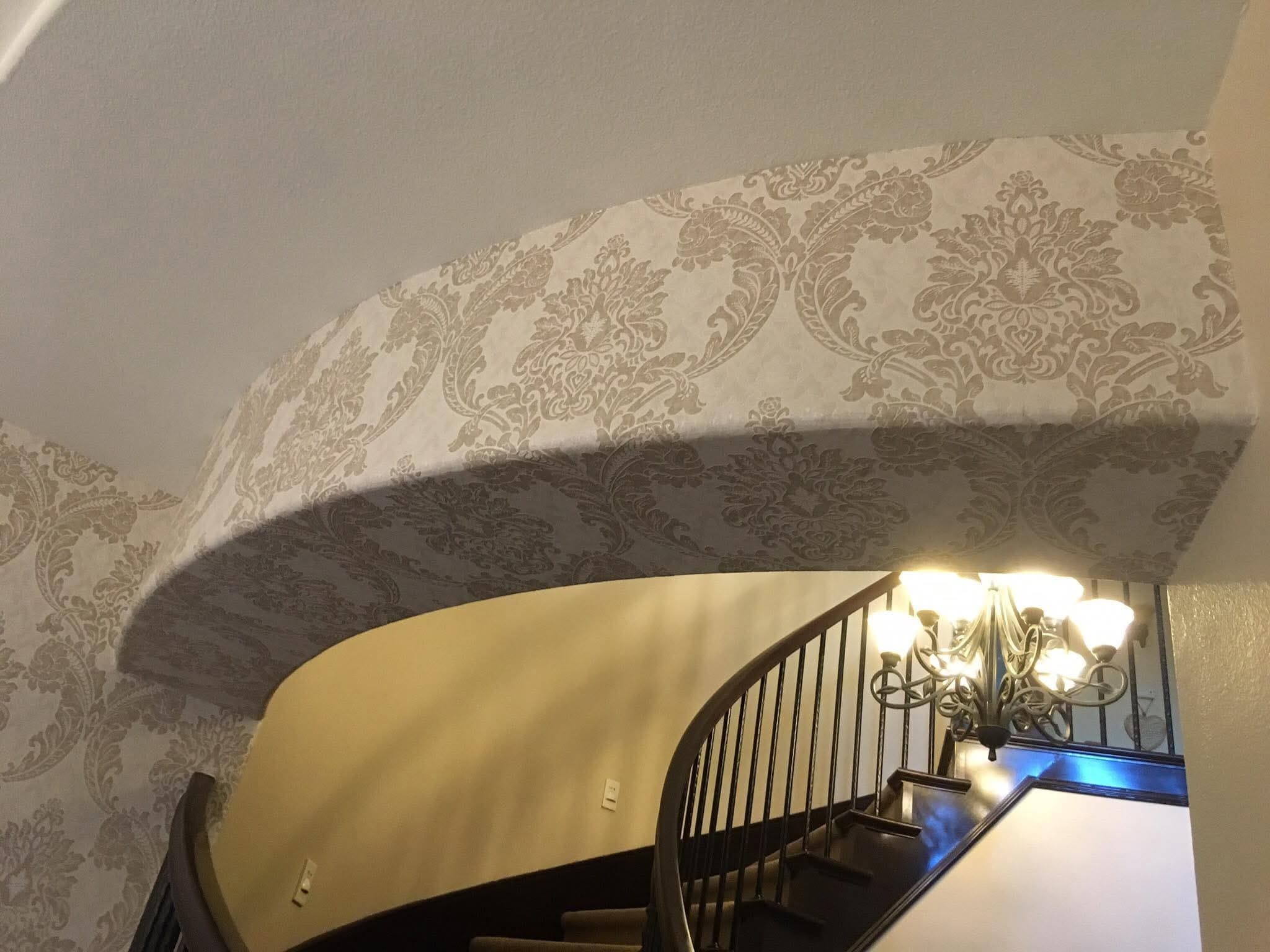 Spiral staircase curved soffit covered in cream and gold floral damask wallpaper