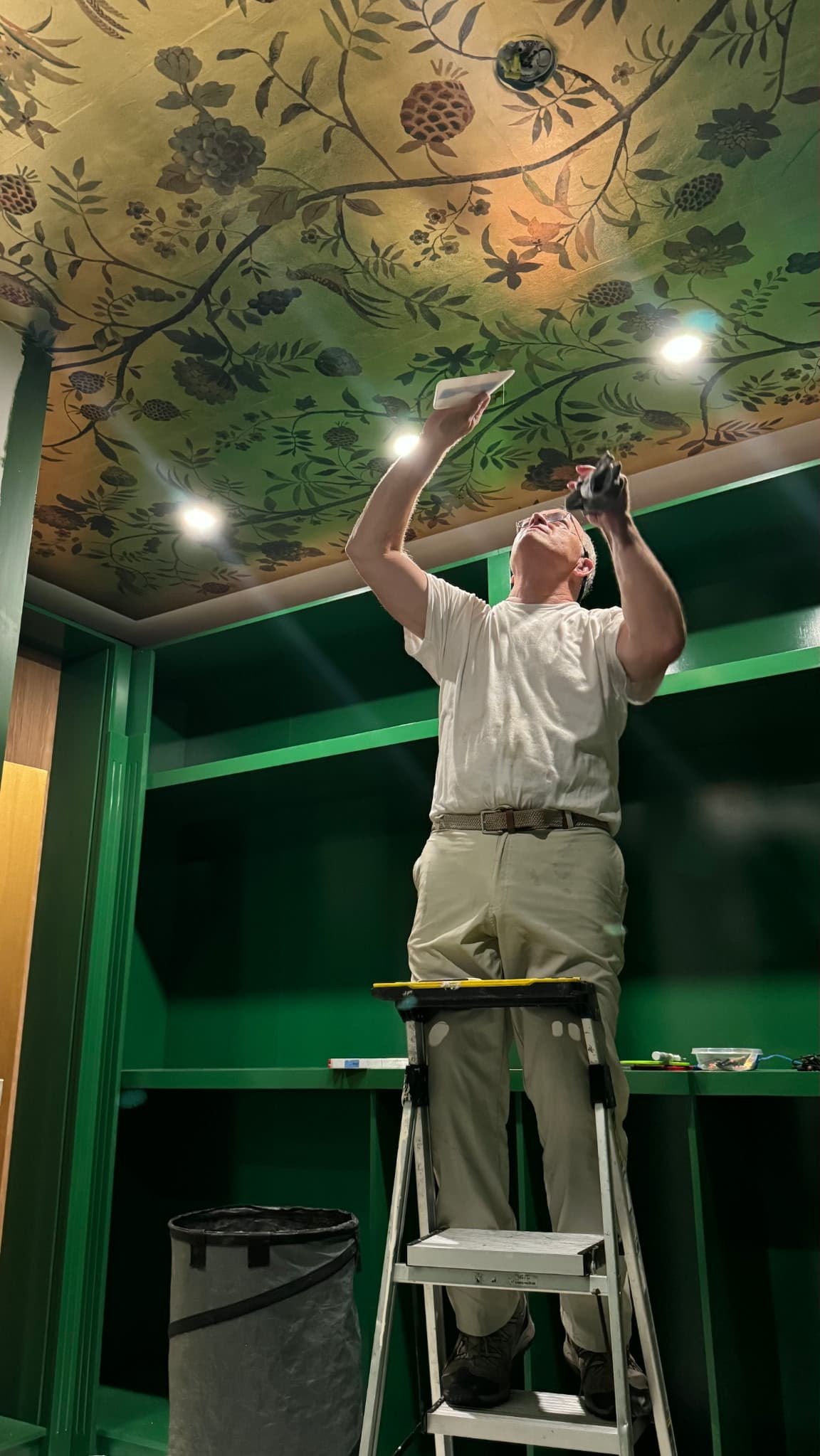 Dan Miller installing gold and green botanical floral wallpaper on a custom closet ceiling in Southern California