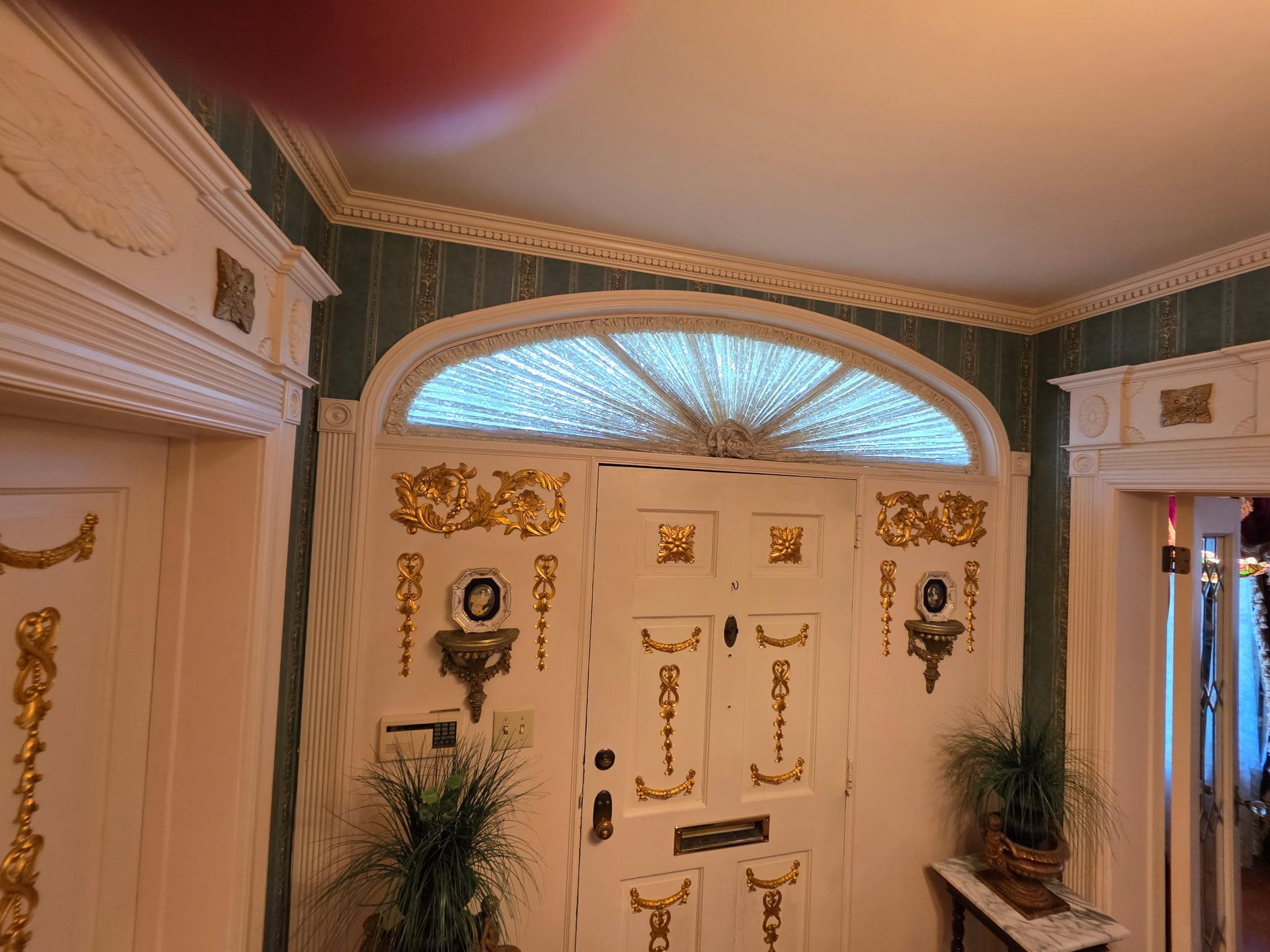 Grand entryway with teal wallpaper, arched transom window and gold door hardware